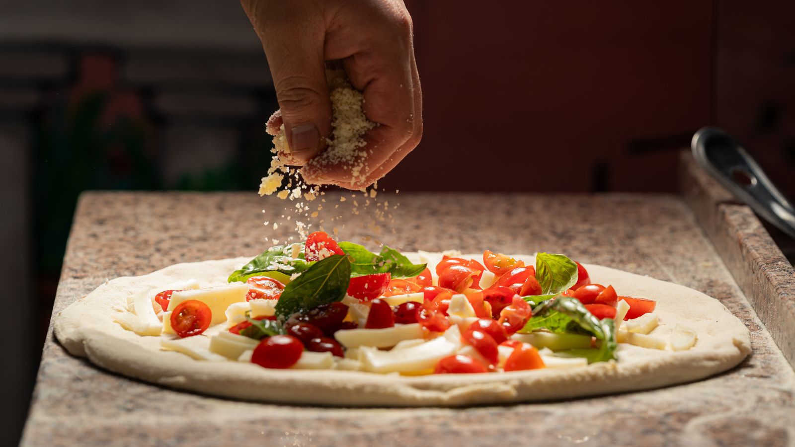 Préparation d'une pizza à la main avec tomates cerises fraîches et basilic